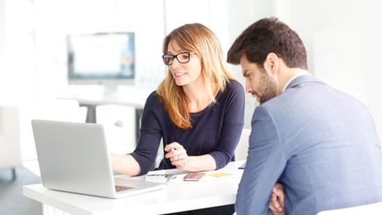 Two business professionals sitting at laptop talking.