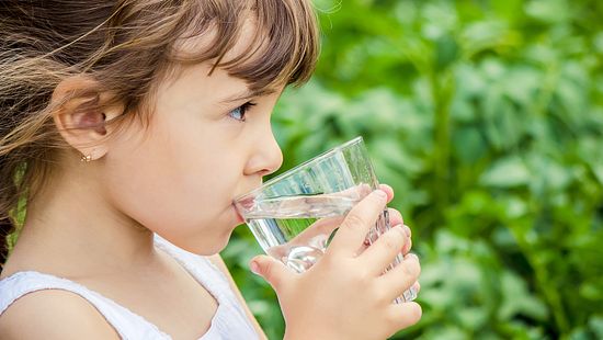 Young girl drinking a glass of water, which demonstrates our drinking water needs.